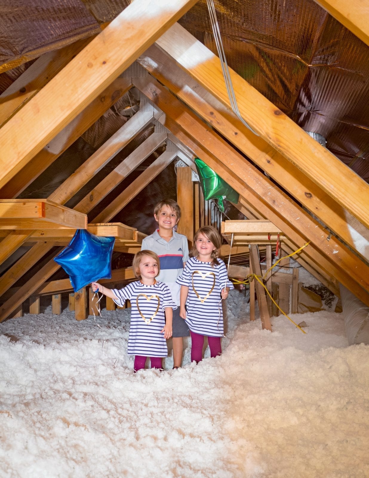 3 kids in an attic holding a blue balloon